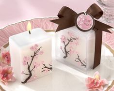 two square candles sitting on top of a plate with pink flowers and a brown ribbon