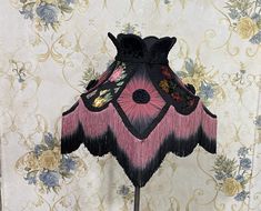 a pink and black lamp on a stand in front of a wallpapered background