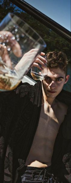 a man drinking from a wine glass in the back seat of a car with his shirt off