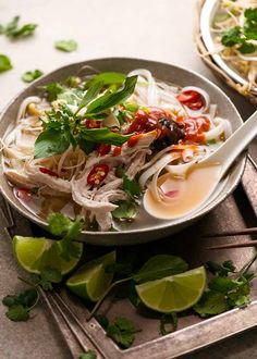 a bowl filled with noodles and garnishes next to a plate of limes