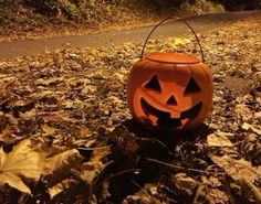 a carved pumpkin sitting on the ground with leaves around it and an empty bucket in front of it