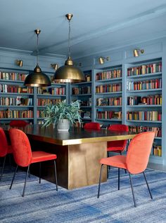 a room filled with lots of books and red chairs next to a wooden table topped with a potted plant