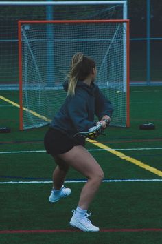 a woman in black jacket and shorts playing with a ball on green field next to goal