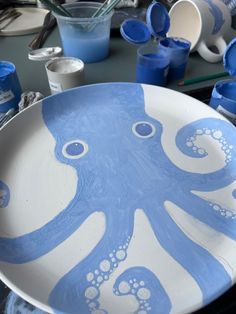 a blue and white plate with an octopus painted on the side, surrounded by paintbrushes