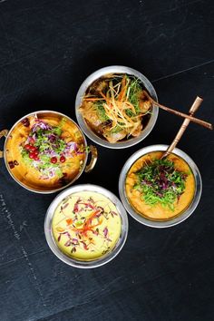 four bowls filled with food sitting on top of a black table next to chopsticks