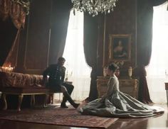 a man and woman sitting on top of a bed in a room with chandelier