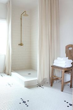 a white bathroom with black and white tile flooring, shower curtain, and wooden chair