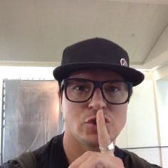 a man wearing glasses and a hat is making a hush sign with his finger while standing in front of a mirror