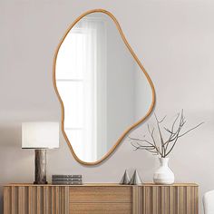 a mirror on the wall above a dresser with a vase and lamp next to it