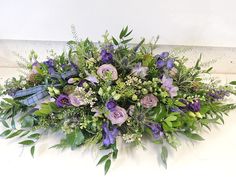 an arrangement of purple flowers and greenery on a white surface