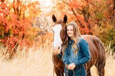 a beautiful young woman standing next to a brown and white horse in a field full of tall grass