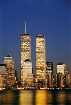 the city skyline is lit up at night with skyscrapers in the foreground and lights reflecting on the water