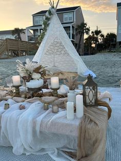 a table topped with candles next to a teepee tent on top of a beach