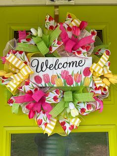 a welcome sign hanging on the front door of a house with flowers and ribbons around it