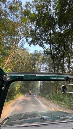 the view from inside a car looking at trees and cars driving down a country road