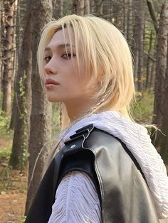 a woman with blonde hair wearing a black leather jacket and white shirt in the woods