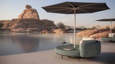 an outdoor seating area with umbrellas and chairs next to the water in front of large rocks