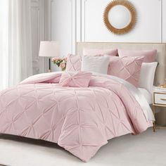 a bed with pink comforter and pillows in a white room next to a window