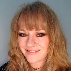 a woman with long blonde hair and piercing on her nose smiles at the camera while wearing a polka dot shirt