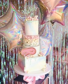 a three tiered cake sitting on top of a table next to balloons and streamers