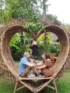 two people sitting in a heart - shaped chair made out of sticks and straws