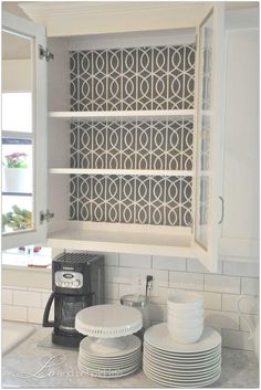 an open cabinet with plates and cups in it on the counter top next to a coffee maker