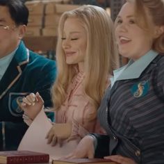 three people sitting at a table with books in front of them and one woman holding a book