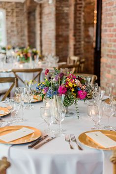 the table is set with gold and white plates, silverware, and floral centerpieces