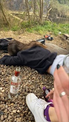 a person laying on the ground next to a bottle of booze and some rocks