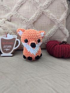 an orange knitted fox sitting on top of a bed next to a cup of coffee