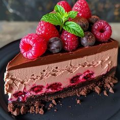 a piece of cake with chocolate and raspberries on top, sitting on a black plate