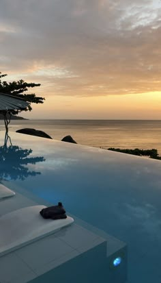 an empty swimming pool with the sun setting over the ocean in the backgroud