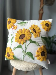 a white pillow with sunflowers on it sitting on a wooden stool next to a potted plant