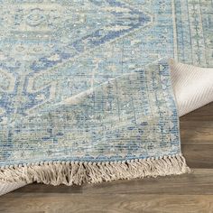 a blue and white rug with fringes laying on top of a wooden floor next to a pillow