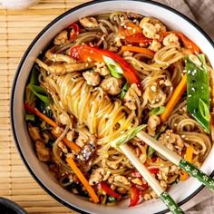 a bowl filled with noodles and vegetables on top of a wooden table next to chopsticks