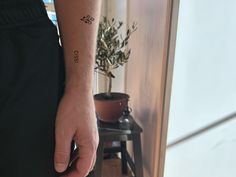 a person with a small tattoo on their left arm, standing next to a potted plant