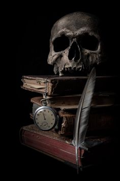 a skull sitting on top of a pile of books next to an old feather quill