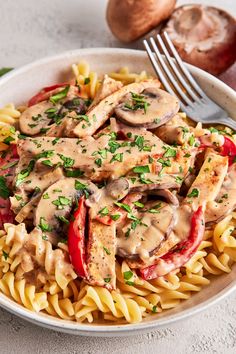 a white bowl filled with pasta covered in mushroom sauce and topped with sliced red peppers