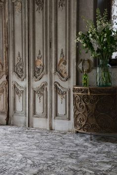 a vase with flowers in it sitting on a table next to two doors and a mirror