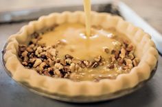 a pie crust is being poured with cheese on top and walnuts in the bottom