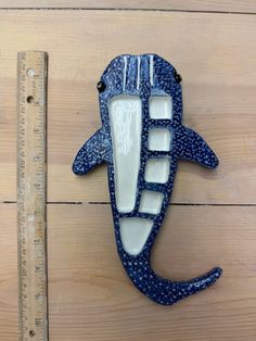 a blue and white seahorse shaped wall decoration next to a ruler on a wooden surface