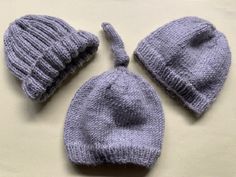 three knitted hats are laid out on a table top, one is grey and the other is light blue