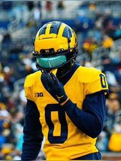 a football player wearing a yellow uniform and holding his hand to his face while standing in front of a crowd