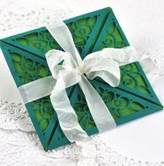 a green box with a white bow on it sitting on top of a doily