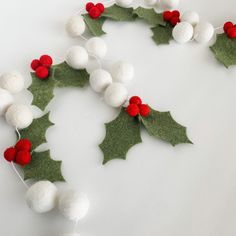 a white and red christmas garland with holly leaves, berries and pom - poms