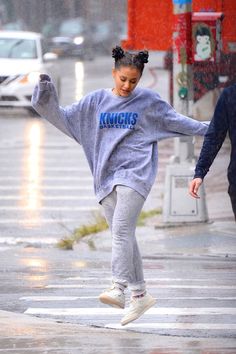 a woman in grey sweatshirt and leggings running down the street with an umbrella