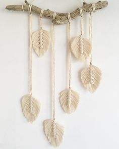 three macrame shells hanging from a twig on a white wall next to a driftwood branch