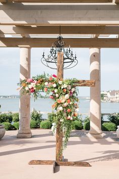 a cross decorated with flowers and greenery in front of the ocean