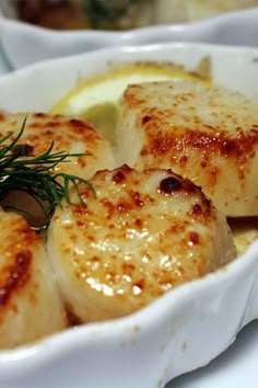 some scallops are in a white dish with lemon wedges and rosemary sprigs