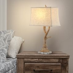 a lamp on a night stand next to a bed with pillows and a couch in the background